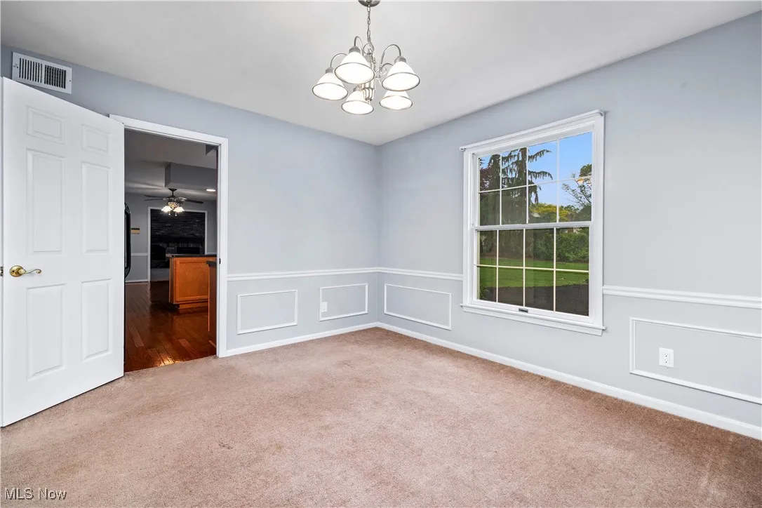 Spare room with carpet floors, a chandelier, and a wainscoted wall