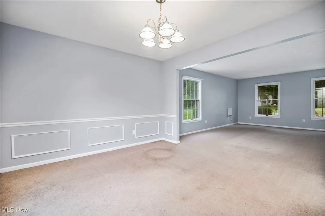 Carpeted empty room featuring a chandelier and baseboards