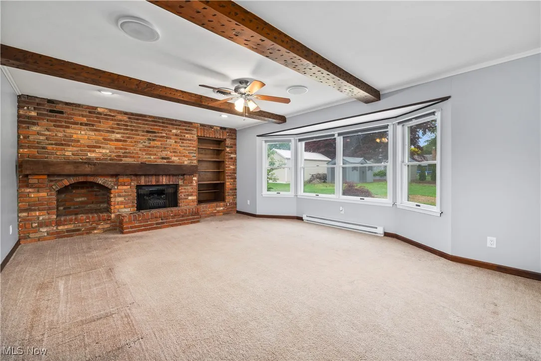 Unfurnished living room with a baseboard radiator, carpet flooring, beamed ceiling, a fireplace, and built in shelves