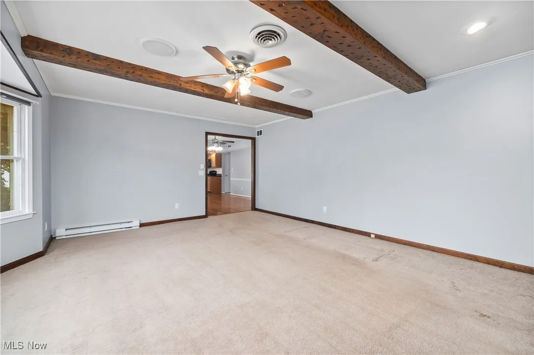 Empty room with baseboard heating, beamed ceiling, ceiling fan, and carpet floors