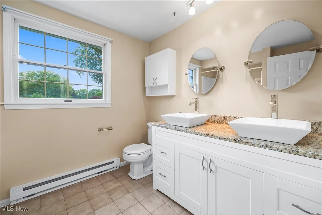 Full bathroom with a baseboard radiator, double vanity, and tile patterned flooring