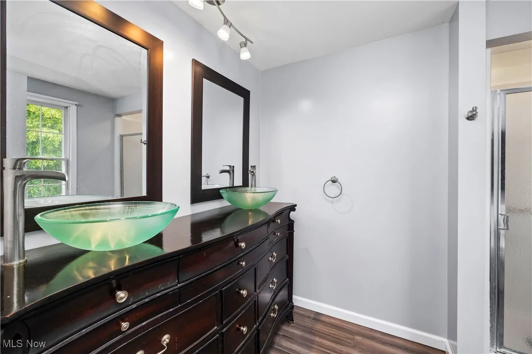 Full bathroom with double vanity, a shower stall, and wood finished floors