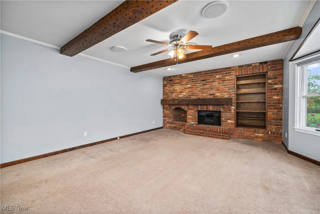 Unfurnished living room featuring beam ceiling, carpet floors, ceiling fan, and a brick fireplace