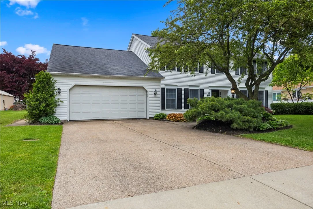 Colonial-style house with a garage, a front yard, concrete driveway, and roof with shingles