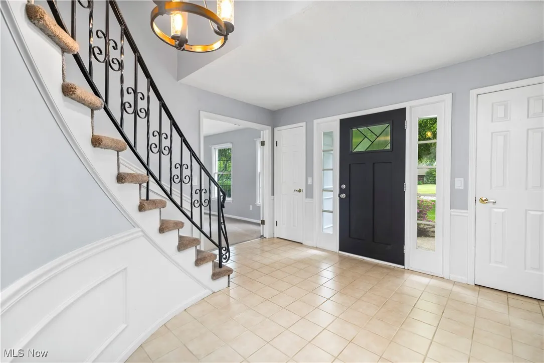 Foyer featuring a chandelier, stairs, light tile patterned flooring, wainscoting, and a decorative wall