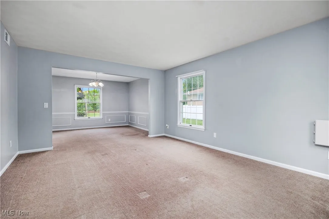 Carpeted empty room featuring a chandelier, plenty of natural light, and a wainscoted wall