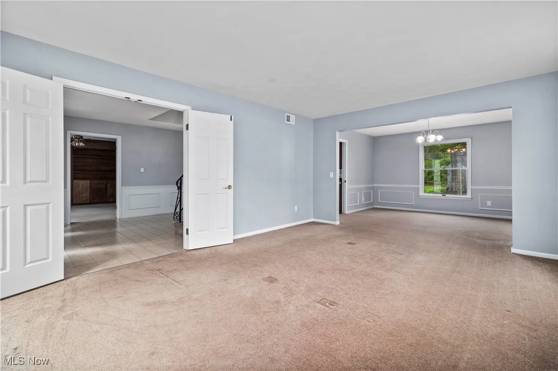 Carpeted spare room featuring a chandelier, wainscoting, and a decorative wall