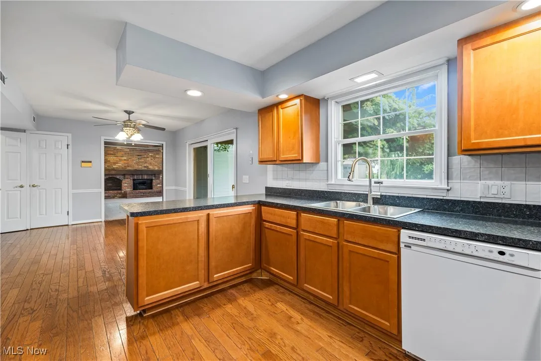 Kitchen with dishwasher, a peninsula, a ceiling fan, hardwood / wood-style flooring, and a fireplace