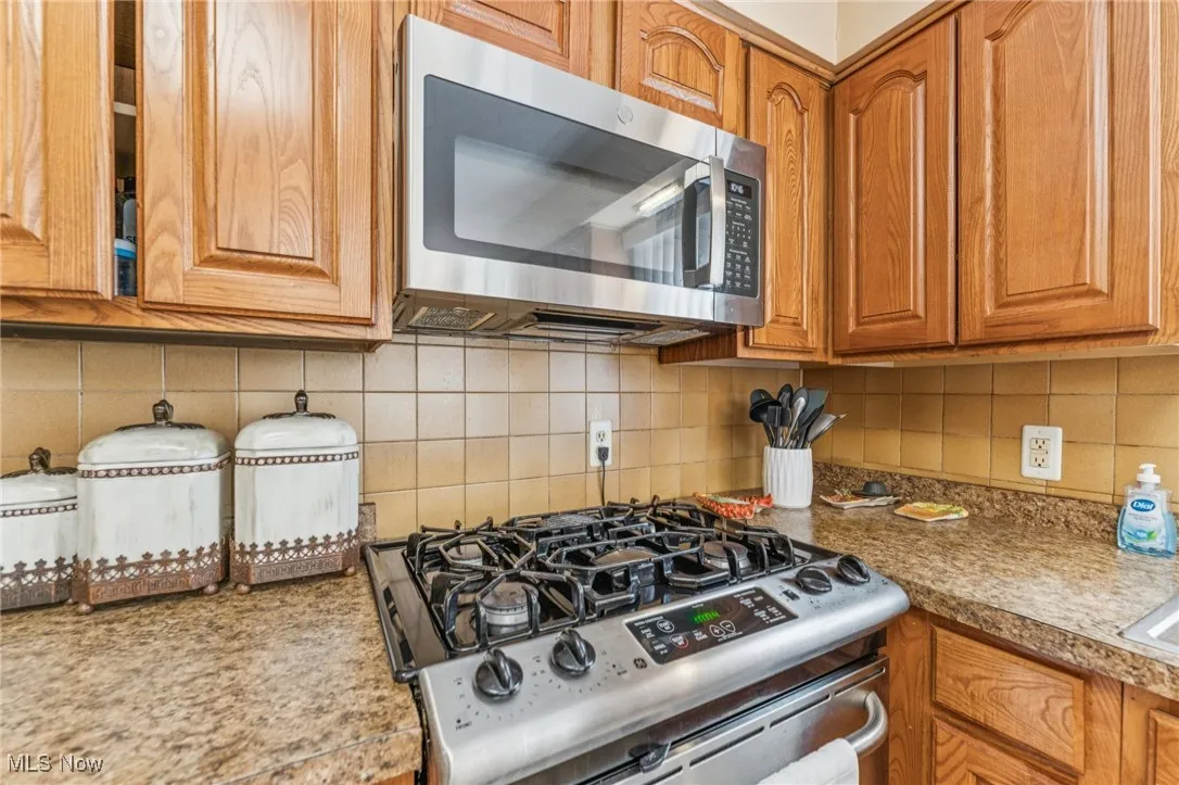 Kitchen with backsplash, stainless steel appliances, brown cabinetry, and light countertops