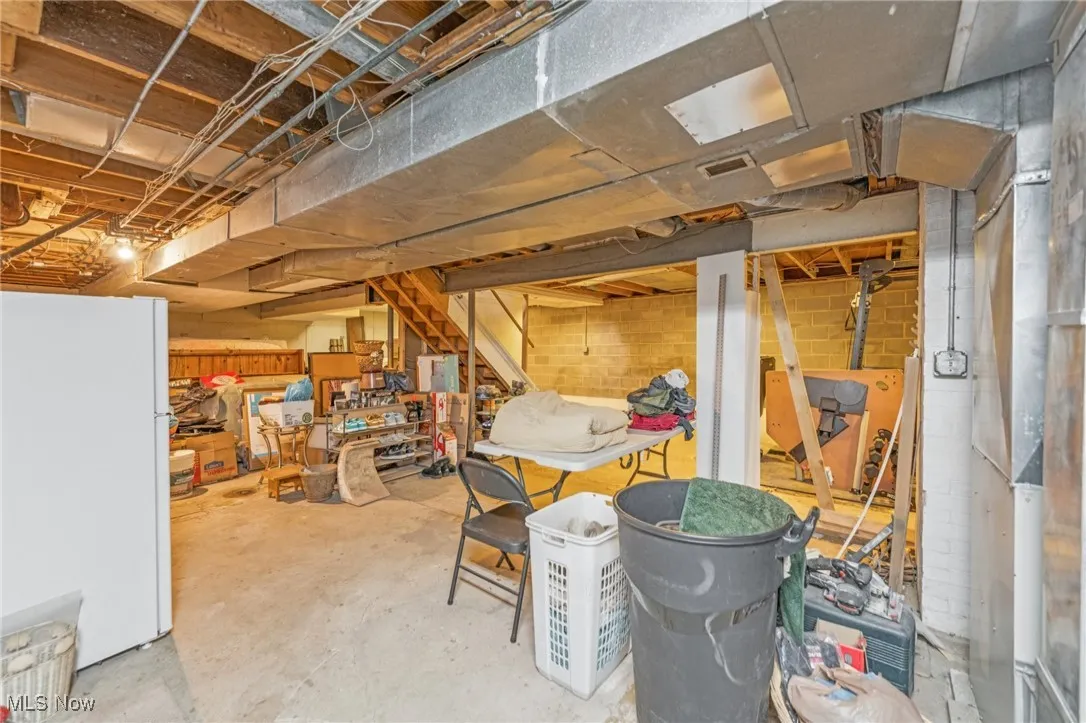 Unfinished basement with freestanding refrigerator and stairs