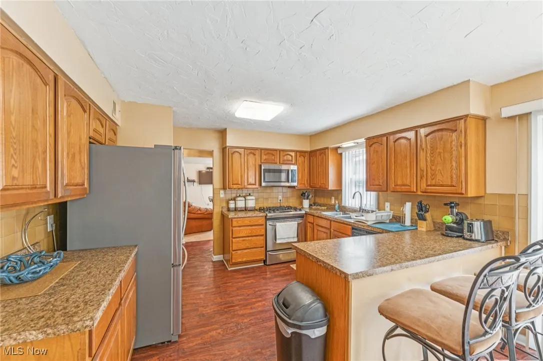 Kitchen with backsplash, dark wood finished floors, a breakfast bar, stainless steel appliances, and a peninsula