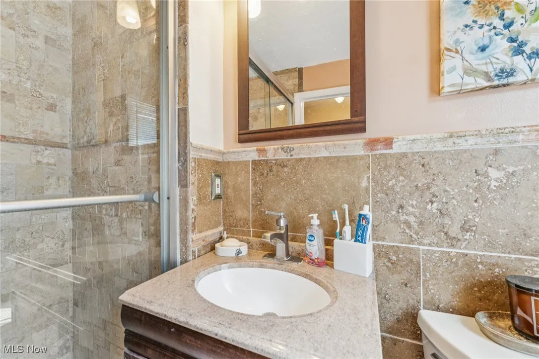 Bathroom featuring tile walls, a stall shower, vanity, and wainscoting