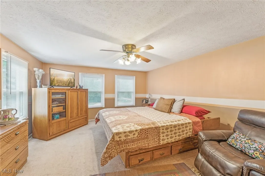 Bedroom with light carpet, a textured ceiling, and ceiling fan