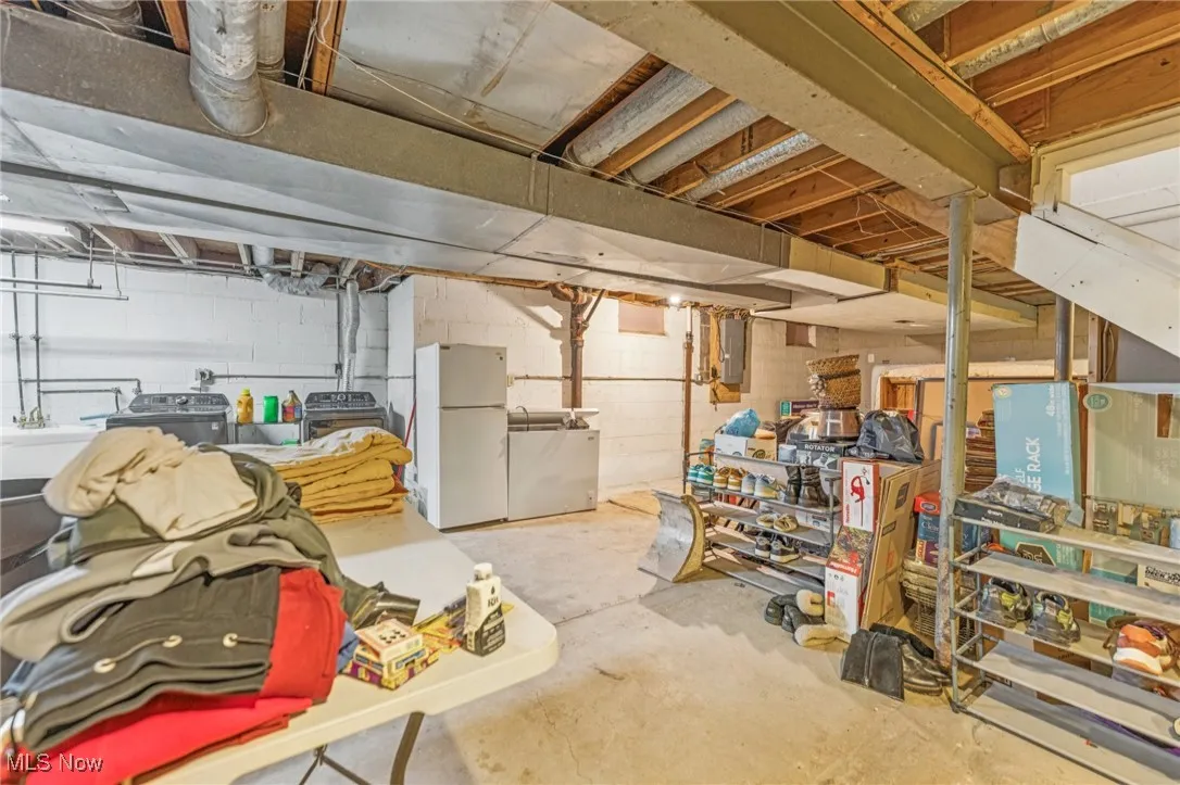 Unfinished below grade area featuring freestanding refrigerator, refrigerator, and electric panel