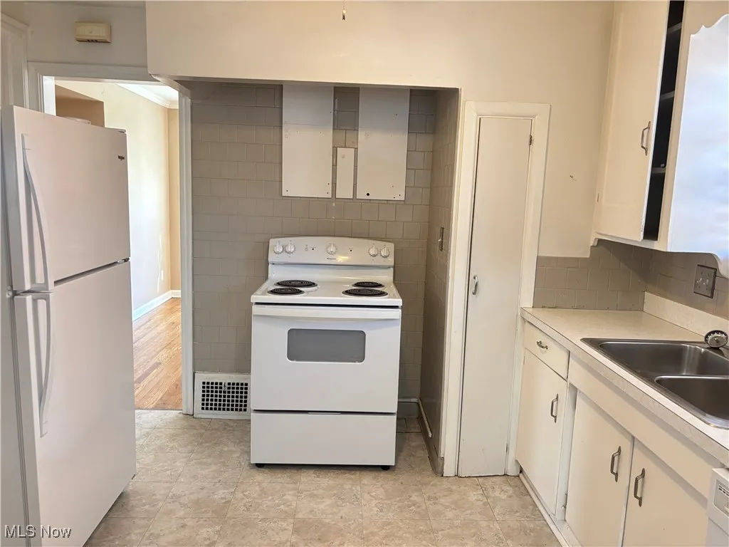 Kitchen with white appliances, light countertops, white cabinetry, and backsplash
