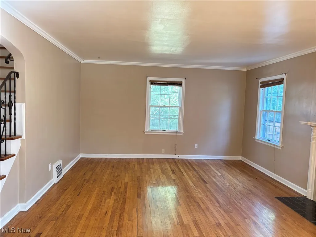 Unfurnished room featuring arched walkways, hardwood / wood-style flooring, stairway, and crown molding