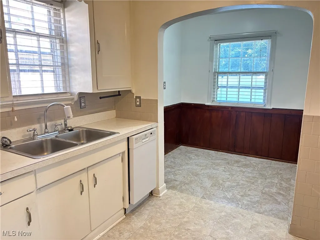 Kitchen with a wainscoted wall, light countertops, wood walls, dishwasher, and arched walkways