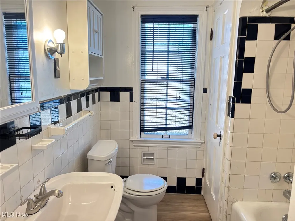 Bathroom featuring tile walls, shower / bath combination, dark wood-style flooring, and a wainscoted wall