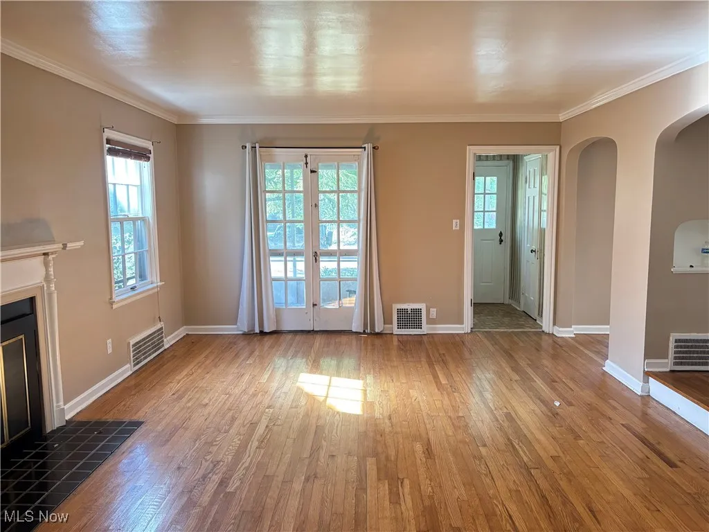 Unfurnished living room with arched walkways, crown molding, a fireplace, plenty of natural light, and hardwood / wood-style floors