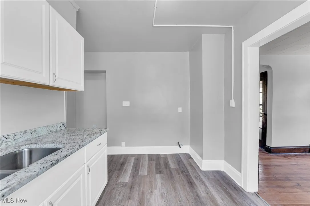 Kitchen featuring light stone countertops, white cabinetry, light wood finished floors, and arched walkways