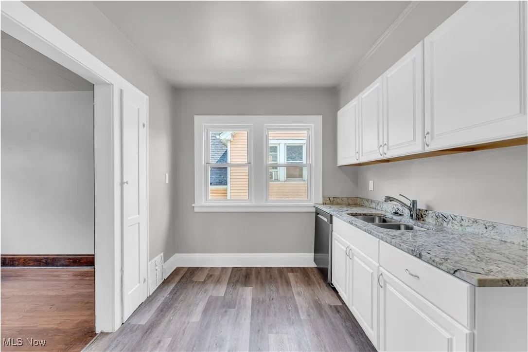 Kitchen featuring white cabinets, light wood-style floors, light stone counters, and stainless steel dishwasher