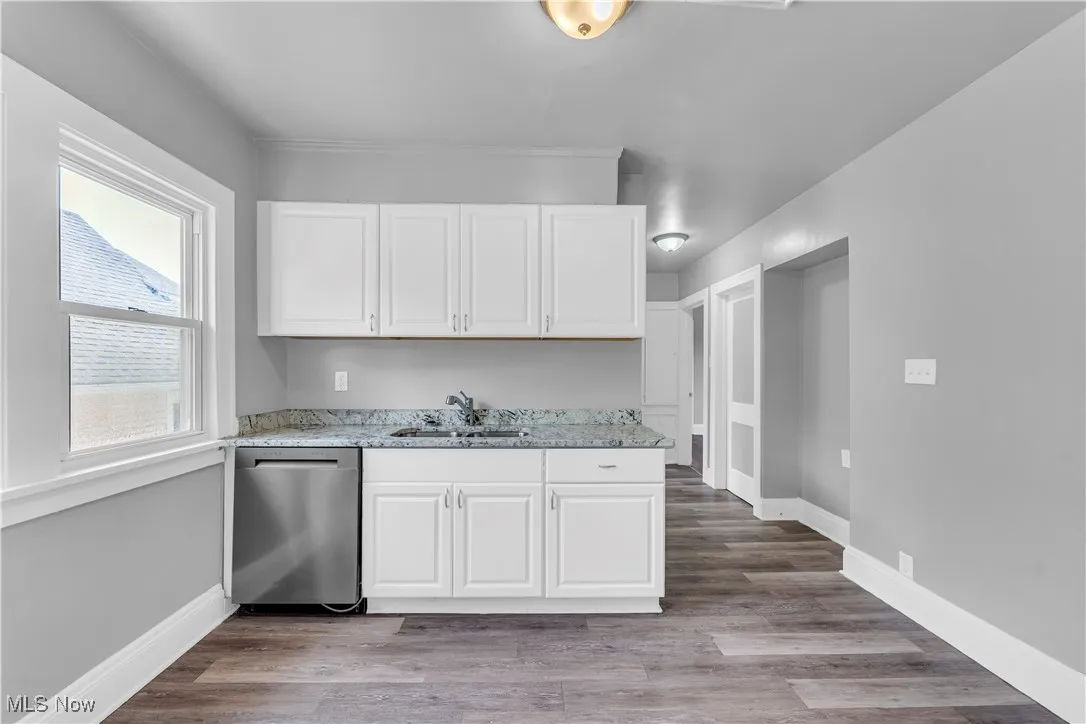 Kitchen with light stone counters, dishwasher, white cabinets, and light wood-style flooring