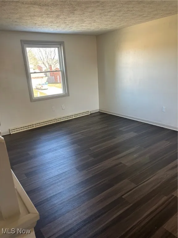 Empty room, dark wood-style flooring, and a textured ceiling