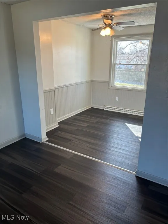 Spare room featuring dark wood style finished floors, ceiling fan, wainscoting