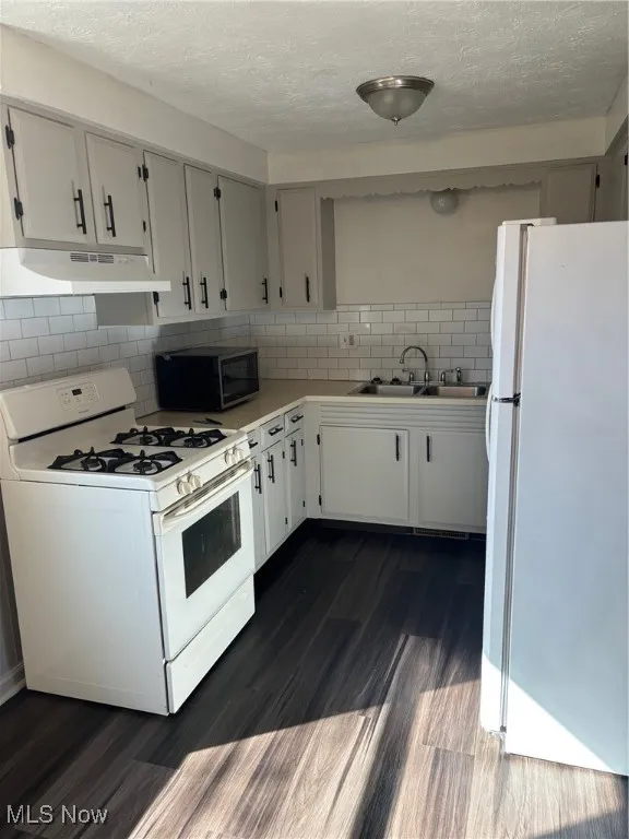 Kitchen with range, refrigerator, light countertops, decorative backsplash, and a textured ceiling