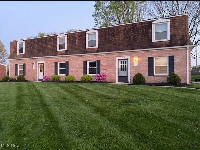 View of front facade featuring mansard roof, a shingled roof, a front lawn, and brick siding