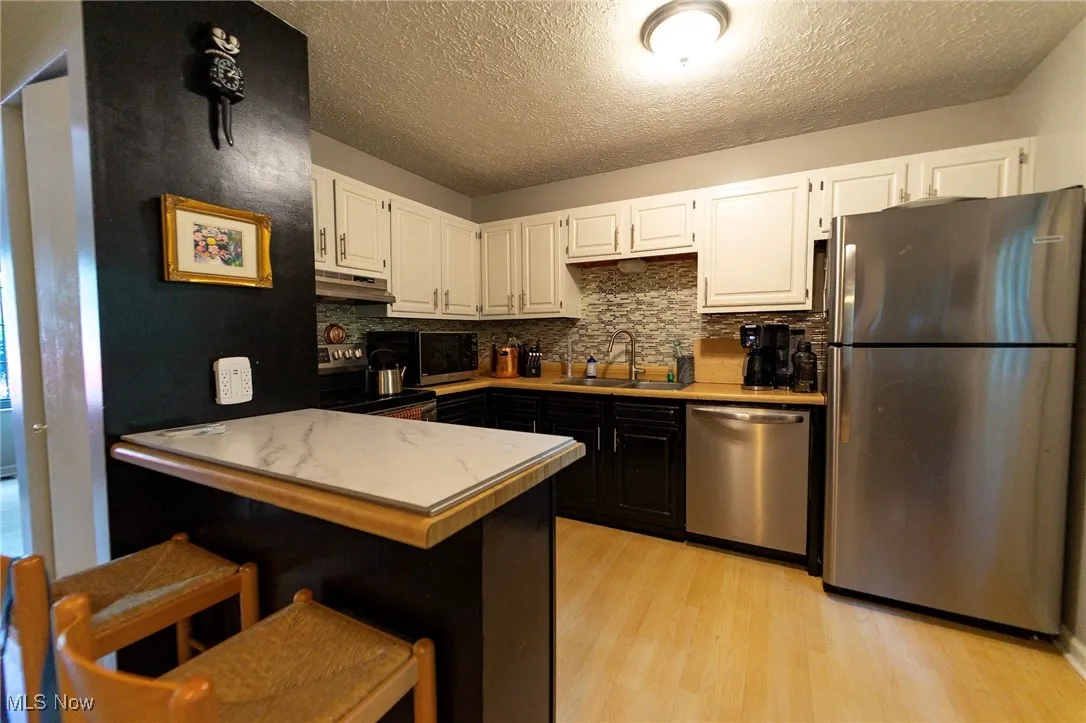 Kitchen featuring stainless steel appliances, white cabinets, light wood-type flooring, backsplash, and light countertops