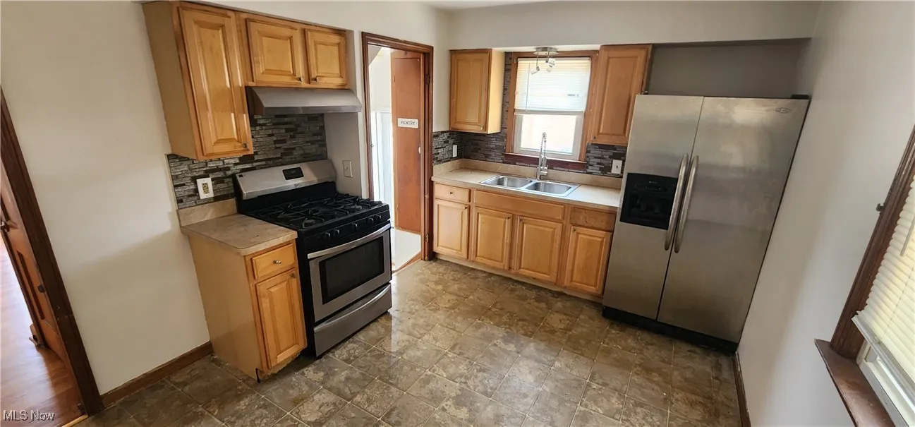 Kitchen featuring appliances with stainless steel finishes, tasteful backsplash, light countertops, under cabinet range hood, and dark stone finish flooring