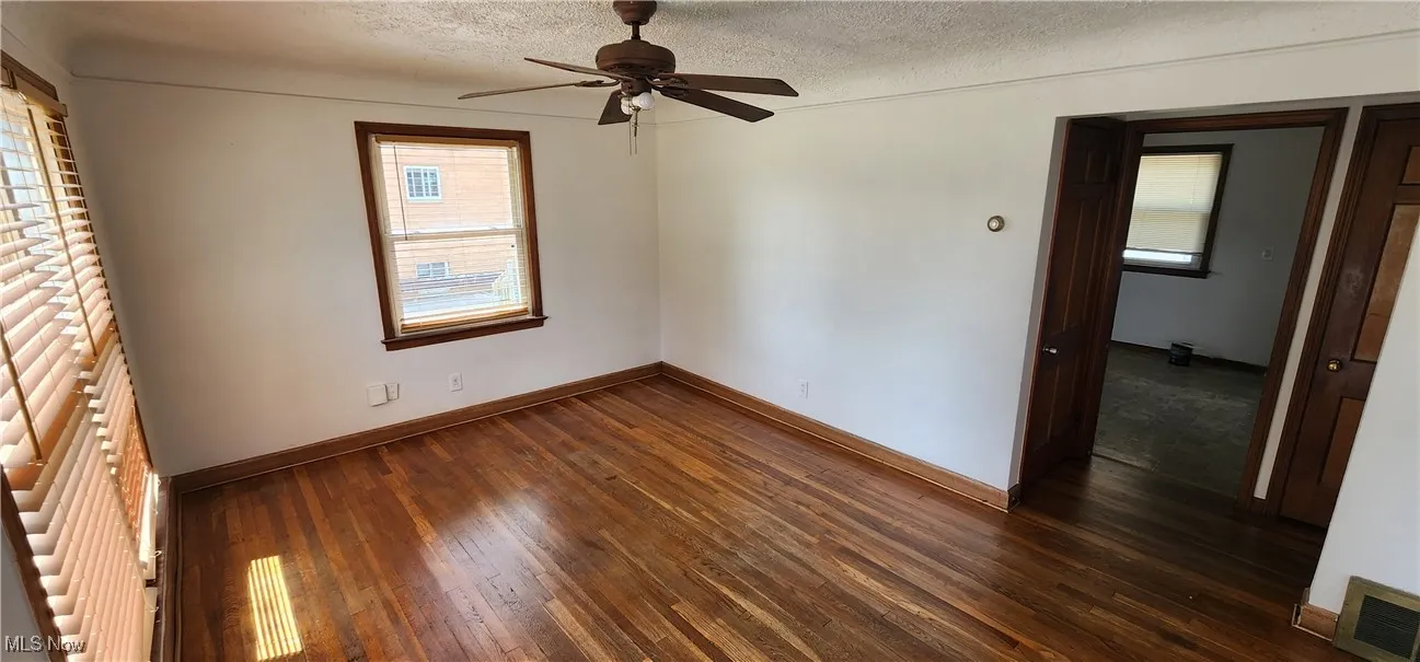 Unfurnished room with dark wood-type flooring, plenty of natural light, a textured ceiling, and a ceiling fan