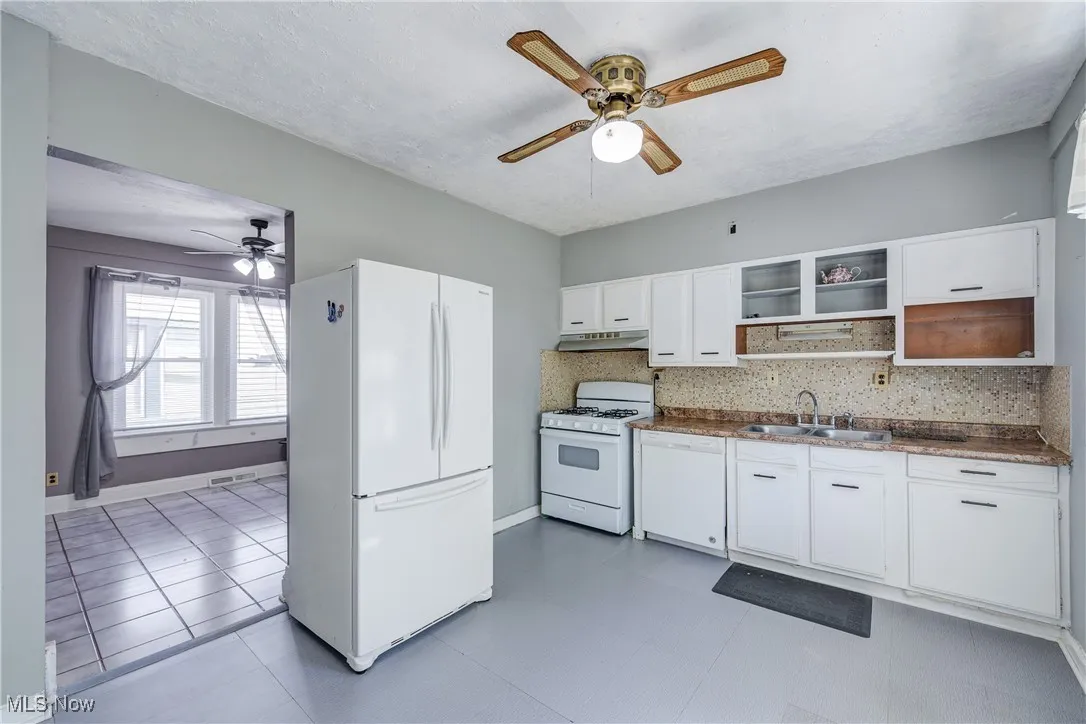 Kitchen featuring white appliances, white cabinetry, ceiling fan, decorative backsplash, and dark countertops