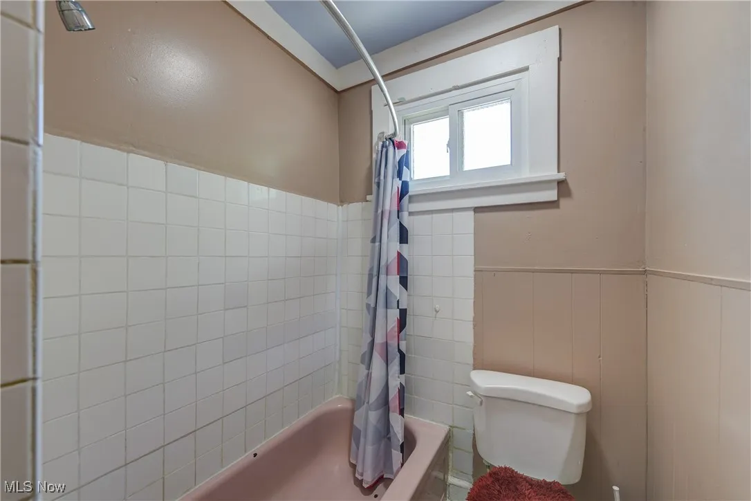 Bathroom with shower / bath combo with shower curtain and a wainscoted wall