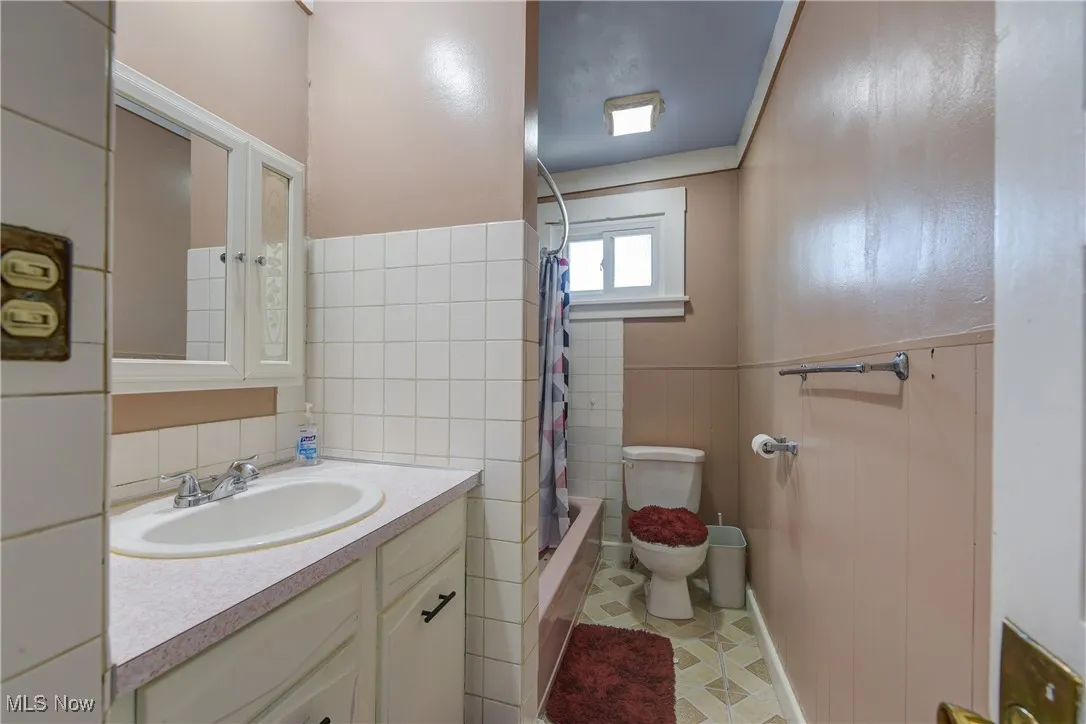 Bathroom featuring vanity, shower / tub combo, wainscoting, and tile walls