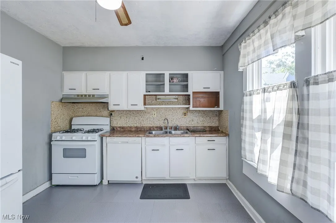 Kitchen with white appliances, dark countertops, white cabinetry, and tasteful backsplash