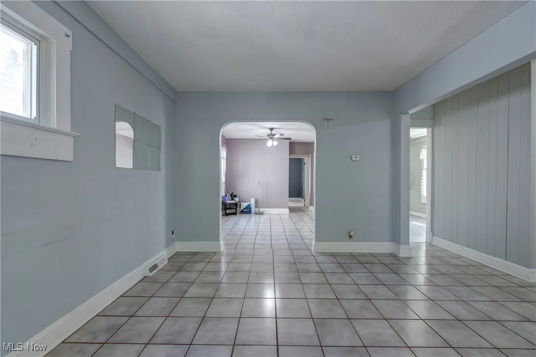 Empty room featuring a ceiling fan, arched walkways, and light tile patterned flooring