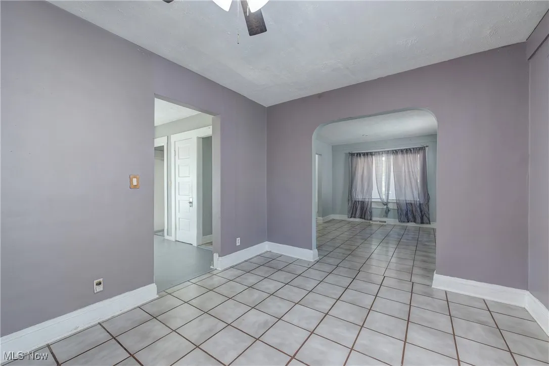 Unfurnished room featuring light tile patterned floors, arched walkways, and a ceiling fan