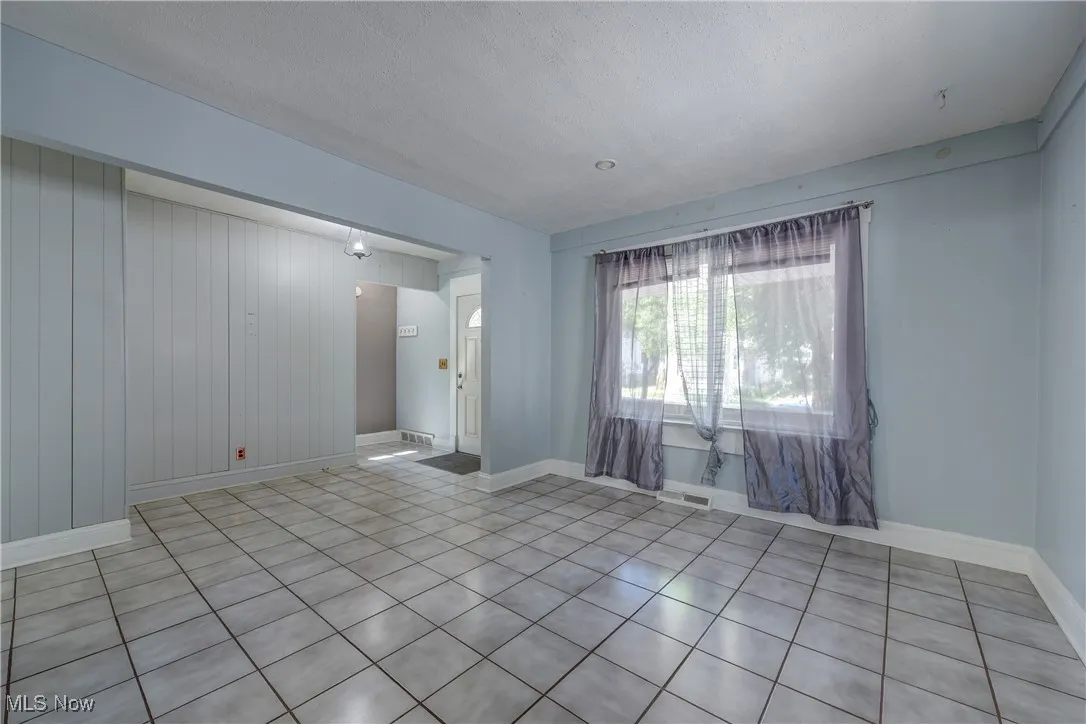 Unfurnished room featuring light tile patterned floors, wooden walls, and a textured ceiling