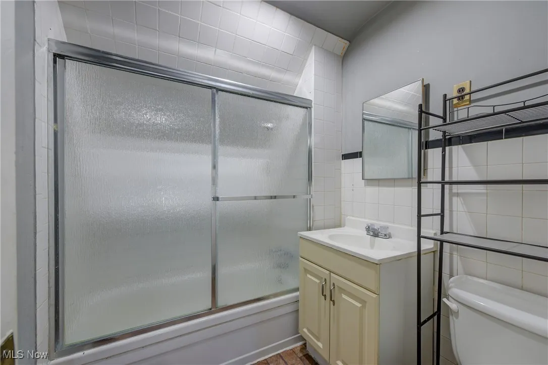 Full bath with tile walls, vanity, and enclosed tub / shower combo