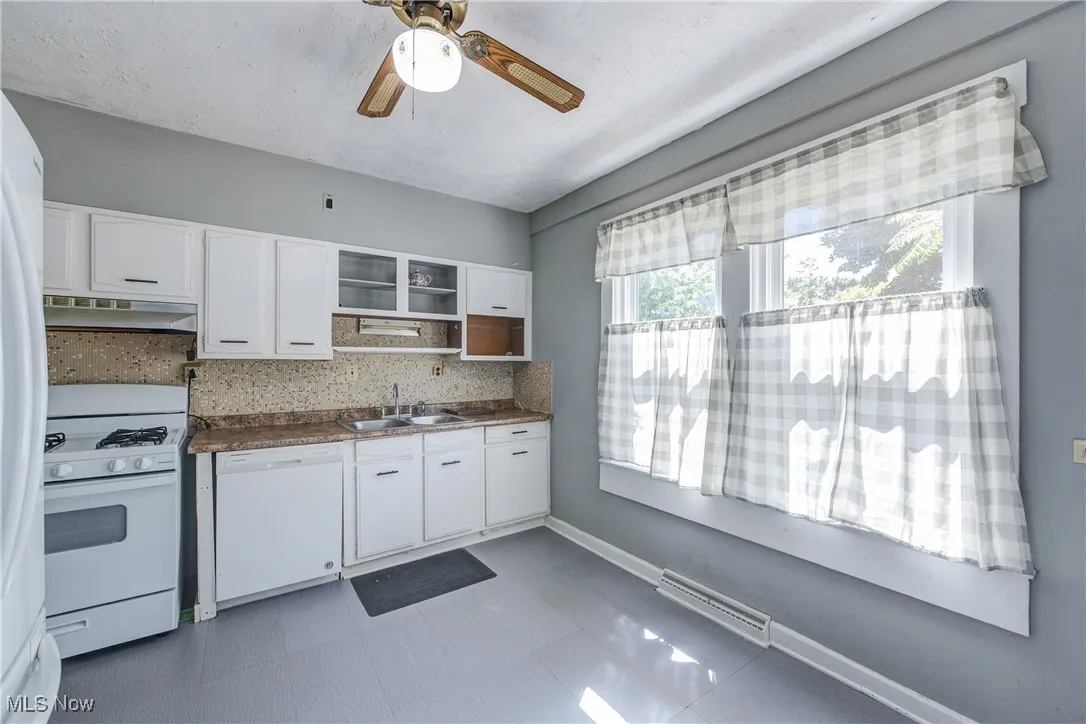 Kitchen featuring dark countertops, white appliances, white cabinets, tasteful backsplash, and under cabinet range hood