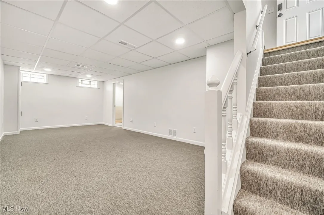 Basement featuring carpet flooring, a drop ceiling, stairs, and recessed lighting