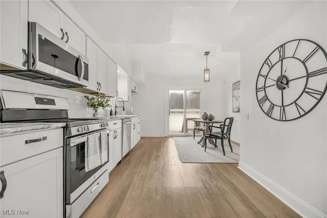 Kitchen featuring stainless steel appliances, white cabinetry, light wood-style floors, backsplash, and pendant lighting