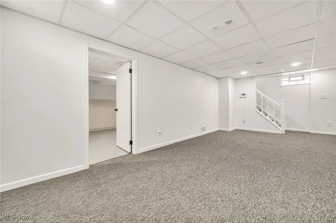 Below grade area with carpet flooring, stairs, and a drop ceiling