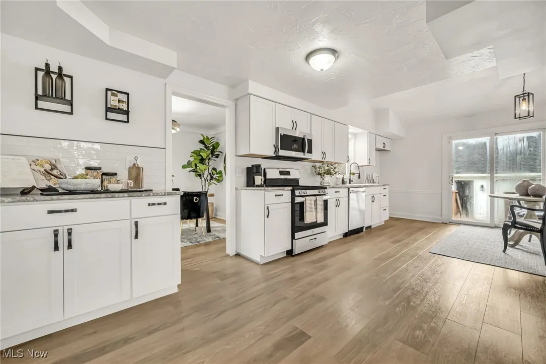 Kitchen with backsplash, stainless steel appliances, white cabinets, light wood finished floors, and a textured ceiling