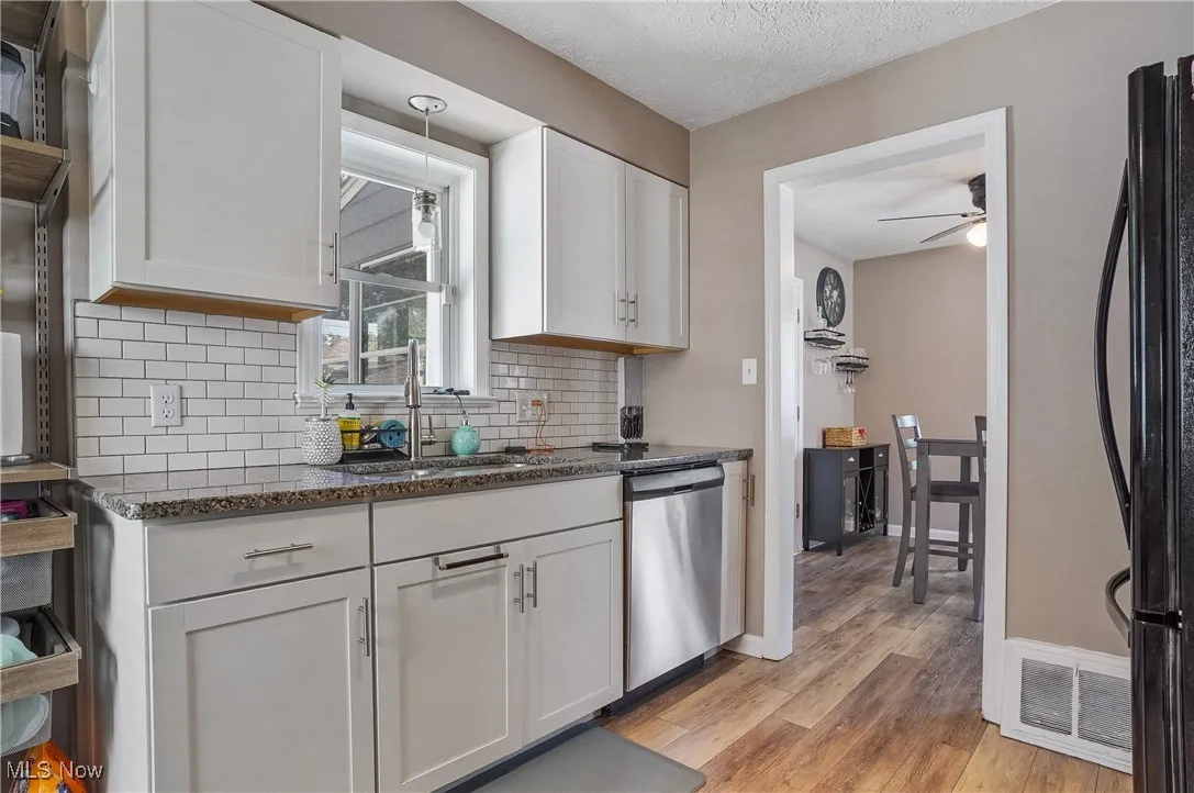 Kitchen featuring white cabinets, dark stone counters, light wood finished floors, decorative backsplash, and dishwasher