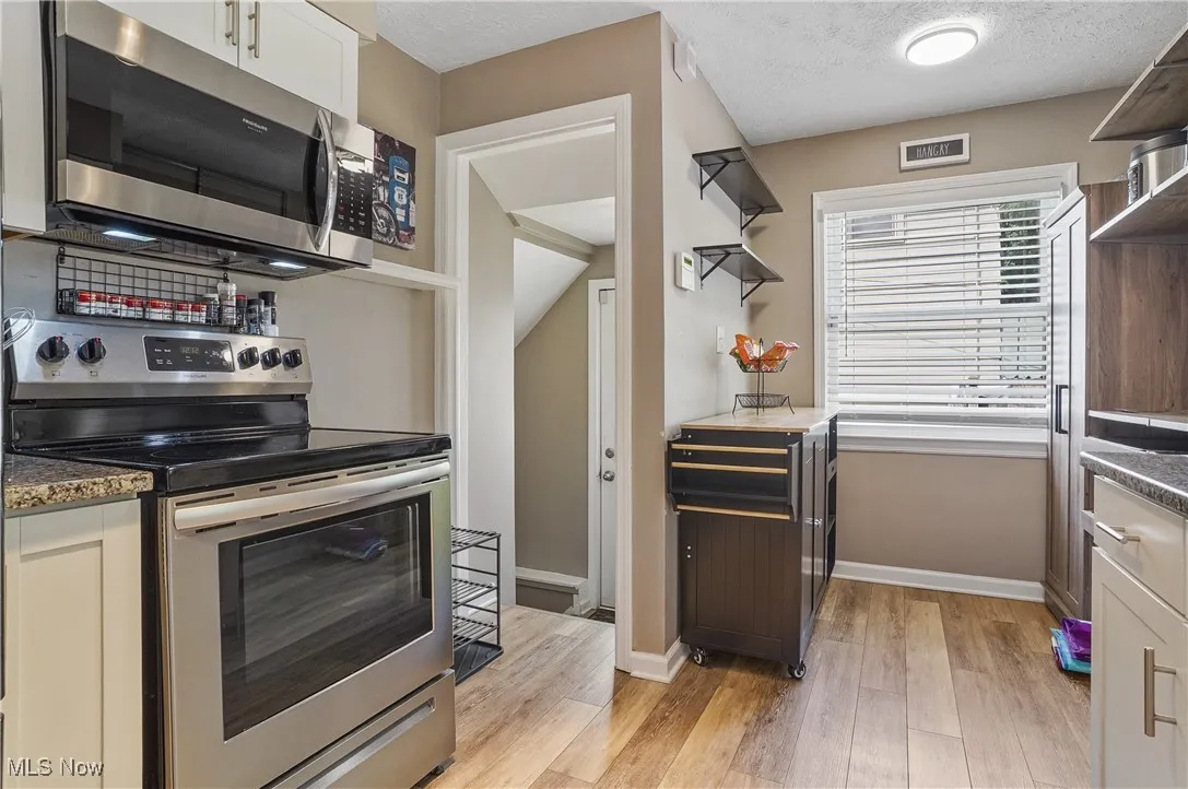 Kitchen featuring open shelves, appliances with stainless steel finishes, light wood-style flooring, a textured ceiling, and dark stone counters