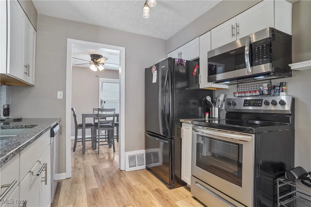 Kitchen with stainless steel appliances, white cabinetry, light wood-style flooring, a textured ceiling, and decorative backsplash