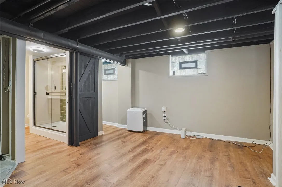 Basement with healthy amount of natural light, light wood finished floors, and a barn door
